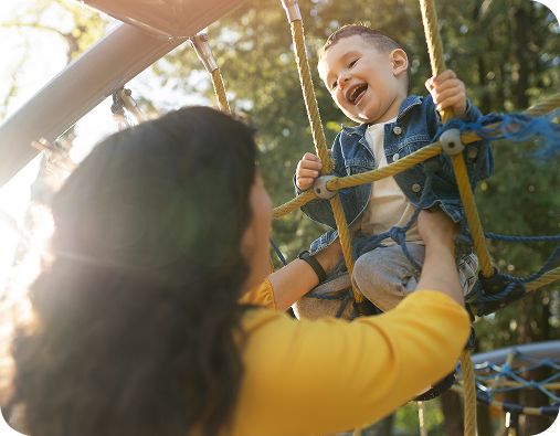 Mujer ayudando a un niño a subir en una red de escalada en un parque infantil, ambos sonriendo.