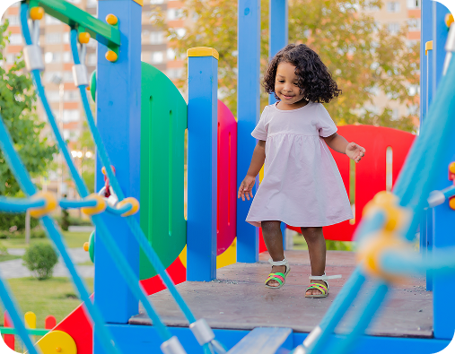 Niña pequeña sonriendo y caminando en un área de juego colorida de un parque infantil.